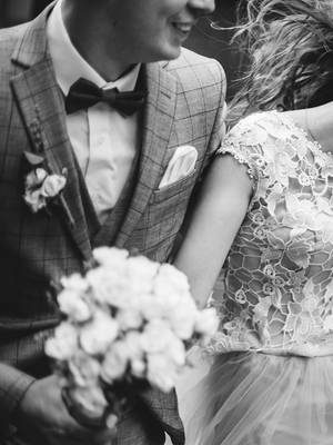 Joyful black and white photo of a laughing bride in a lace dress and tiara, with her groom in a patterned suit holding a bouquet, during their Micro Wedding at Rixos Pera Istanbul.